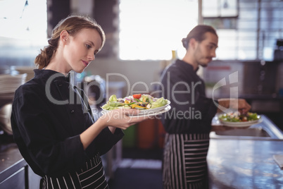 Young wait staff holding fresh salad plates while standing in commercial kitchen