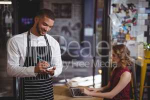 Smiling young waiter writing in notepad while standing at coffee shop