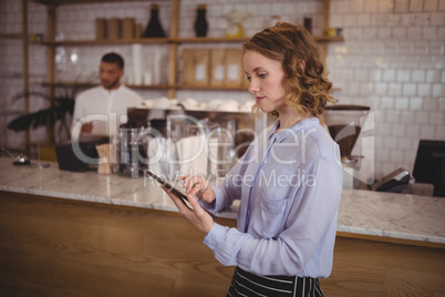 Young pretty waitress using digital tablet while standing by counter