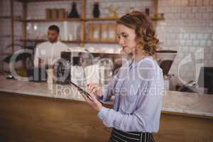 Young pretty waitress using digital tablet while standing by counter