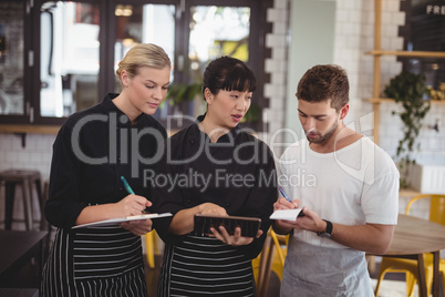 Young waiter and waitress discussing over digital tablet