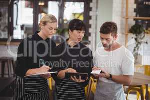 Young waiter and waitress discussing over digital tablet