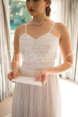 Beautiful bride holding wedding card at home