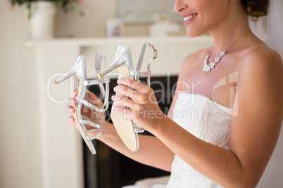 Midsection of smiling bride holding sandals in fitting room