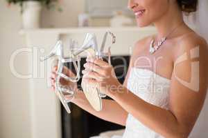 Midsection of smiling bride holding sandals in fitting room
