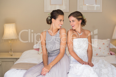 Happy bride and bridesmaid while sitting on bed at home