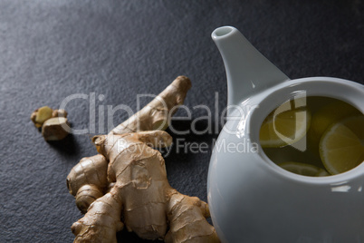 Lemon slice in teapot with ginger on black background
