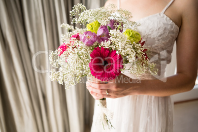 Midsection of bride in wedding dress holding bouquet at home