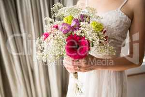 Midsection of bride in wedding dress holding bouquet at home