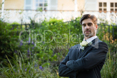 Portrait of handsome bride with arms crossed standing in park