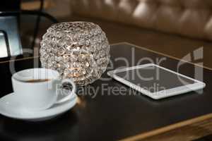 Close-up of coffee, digital tablet and lit candle on table