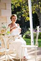 Beautiful bride having coffee on chair in yard