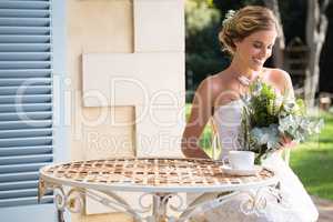 Beautiful bride looking at bouquet while sitting on chair