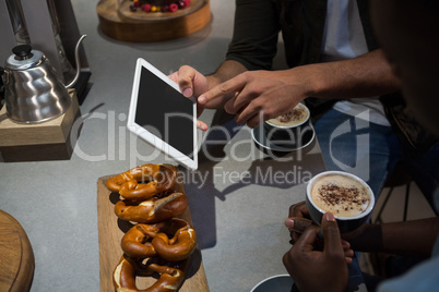 Mid section of man using digital tablet while having coffee