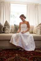 Beautiful bride writing in diary while sitting on sofa