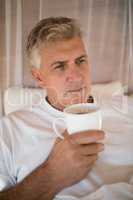 Thoughtful man having coffee on bed