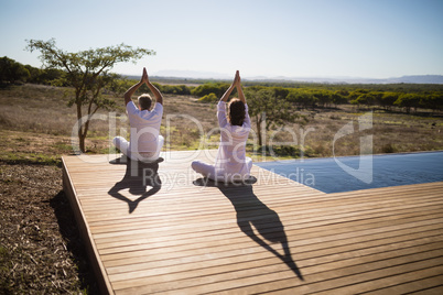 Rear view of couple practicing yoga on wooden plank