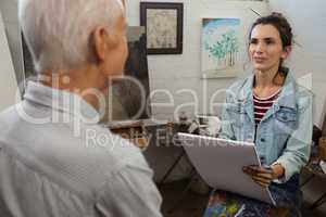 Woman interacting with senior man while sketching on canvas