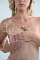 Mid section of Shirtless woman checking for lumps while examining breast