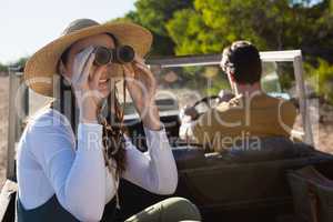 Woman using binocular with man driving off road vehicle
