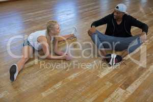 Full length of female dancer with friend stretching legs on floor