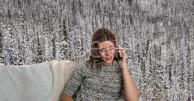 Woman with warm jumper on phone on couch in front of snow forest