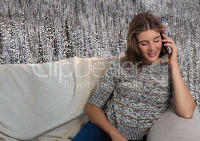 Woman with warm jumper on phone on couch in front of snow forest