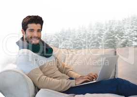 Man with scarf on laptop on couch in snow forest