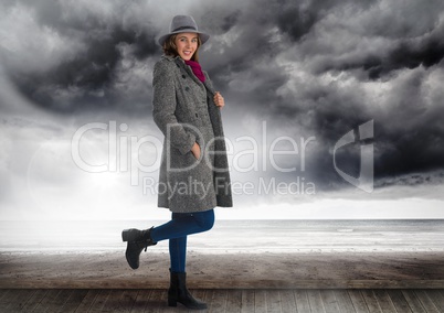 Woman in hat and warm clothes under dark clouds and sea