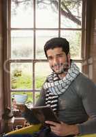 Man wearing scarf with tablet and cup by window in countryside