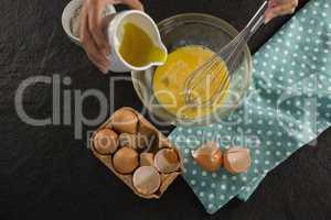 Woman adding oil into beaten eggs in a bowl
