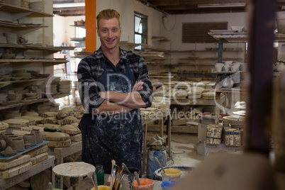 Male potter standing with arms crossed in pottery workshop