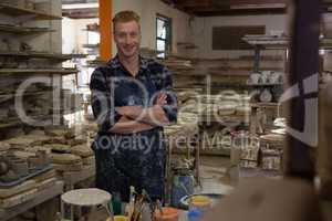 Male potter standing with arms crossed in pottery workshop