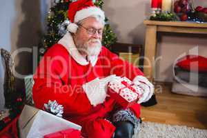 Santa claus sitting on rug and looking at gift box in living room