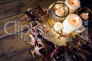 Lit candles and dry leaves on table