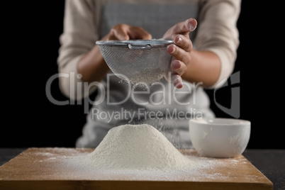 Woman sieving flour from the bowl on the wooden board