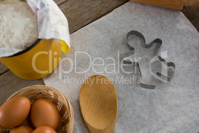 Butter paper, flour, rolling pin cookie cutter and eggs kept over a wooden table