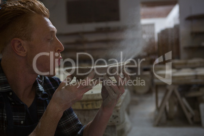 Male potter blowing dust from a bowl