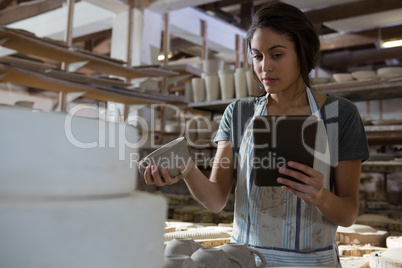 Female potter holding cup while using digital tablet