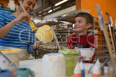 Female potter interacting with boy while painting bowl