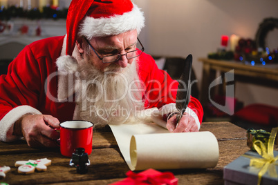 Santa Claus having coffee while writing on scroll
