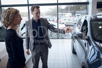 Salesman showing car to female customer in showroom