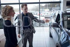 Salesman showing car to female customer in showroom