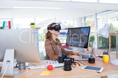 Female executive working on laptop while using virtual reality headset