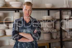 Male potter standing with arms crossed in pottery workshop