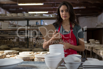 Confident female potter standing with clipboard