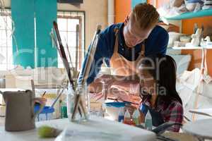 Male potter assisting girl to paint bowl