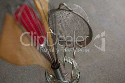 Whisker, wooden spoon, strainer and spatula on glass jar