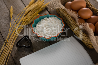 Book, eggs, flour, cookie cutter and wheat stem kept on a table