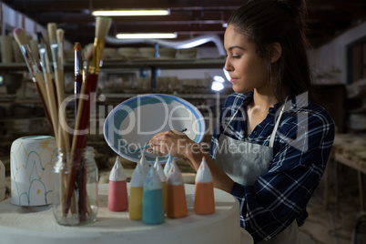 Female potter decorating bowl with paint brush